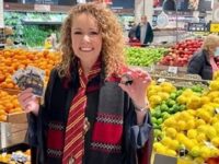 Lisa Ronson stands in front of the produce section in a Coles supermarket holding products in her hands.