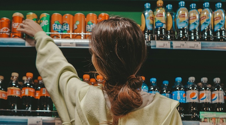 A woman reaching for a can of soda on a supermarket shelf