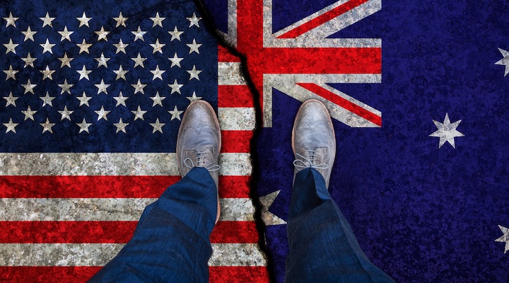 Business man stands on cracked flags of USA and Australia.