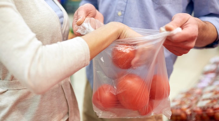 close up of couple with plastic bag buying tomatoes at grocery store or supermarket